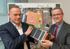 Sascha Kelterborn von der Firma Microvast (links) und Andreas Igel (SPD), Bürgermeister von Lud-wigsfelde, präsentieren bei der Bekanntgabe der Ansiedlung des US-Betriebes einen Batteriespeicher.