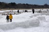 Spaziergänger gehen am Ostseestrand von Zingst über meterhohe Eis- und Schneehaufen.
