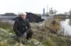 Hans Brammer hockt auf dem Wall von Abfallmaterialien, im Hintergrund: das Asphaltmischwerk Demmin. Das Versickerungsbecken ist viel zu nahe an der Grundstücksgrenze gebaut worden, so ein Vorwurf.