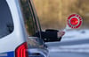 Eine Polizistin hält eine Anhaltekelle aus dem Seitenfenster eines Einsatzfahrzeugs.